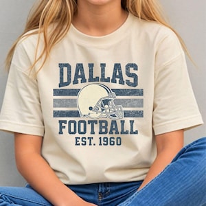 A woman wearing a t-shirt with a graphic design of a football helmet and the text "DALLAS FOOTBALL EST. 1960" printed on it.