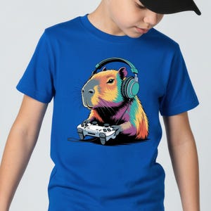 A boy wearing a blue t-shirt with a colorful cartoon image of a capybara wearing headphones and holding a video game controller.