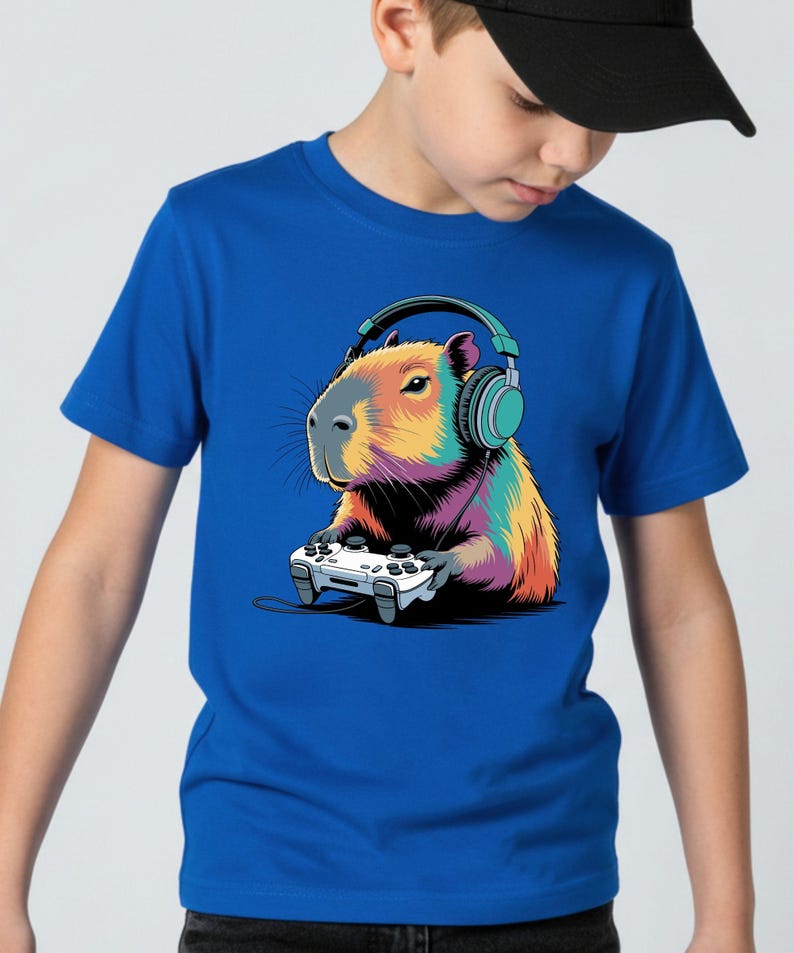 A boy wearing a blue t-shirt with a colorful cartoon image of a capybara wearing headphones and holding a video game controller.