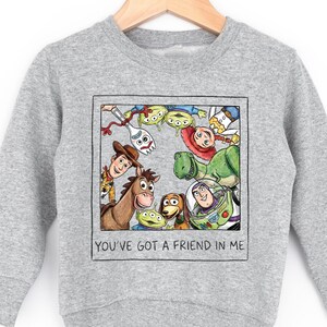 A gray sweatshirt with a graphic design featuring characters from the Toy Story movie, including Woody, Buzz Lightyear, and other beloved characters.