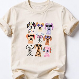 A white t-shirt with a graphic design of nine colorful dog faces wearing sunglasses.