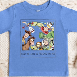 A blue t-shirt with a graphic design featuring characters from the Toy Story movie, including Woody, Buzz Lightyear, and other beloved characters.