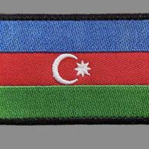 May include: Embroidered patch featuring the flag of Azerbaijan. The rectangular patch has horizontal stripes of blue, red, and green. A white crescent moon and eight-pointed star are centered on the red stripe. The patch is bordered by a black frame.
