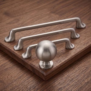 Peut inclure: Une collection de quincaillerie d'armoire en nickel brossé comprenant trois poignées de tiroir allongées de longueurs variables et un bouton d'armoire sphérique. Chaque pièce présente une finition métallique lisse avec des bases de montage incurvées.