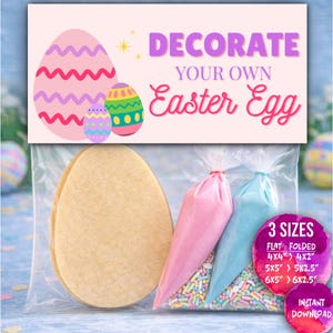 May include: An Easter egg decorating kit in a clear bag. The kit includes two egg-shaped biscuits, pink and blue icing bags, and sprinkles. The packaging features the text "DECORATE YOUR OWN Easter Egg" and details three sizes.