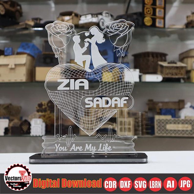 May include: A clear acrylic heart-shaped decorative piece with the names "ZIA" and "SADAF" etched on it. The design includes a silhouette of a couple, roses, and the phrase "You Are My Life". The base is black.