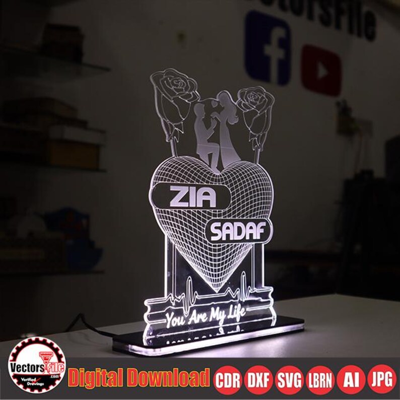 May include: A lighted heart-shaped decorative piece with the names "ZIA" and "SADAF" displayed. The design includes a couple silhouette, roses, and the phrase "You Are My Life". The base is black, and the light is white.