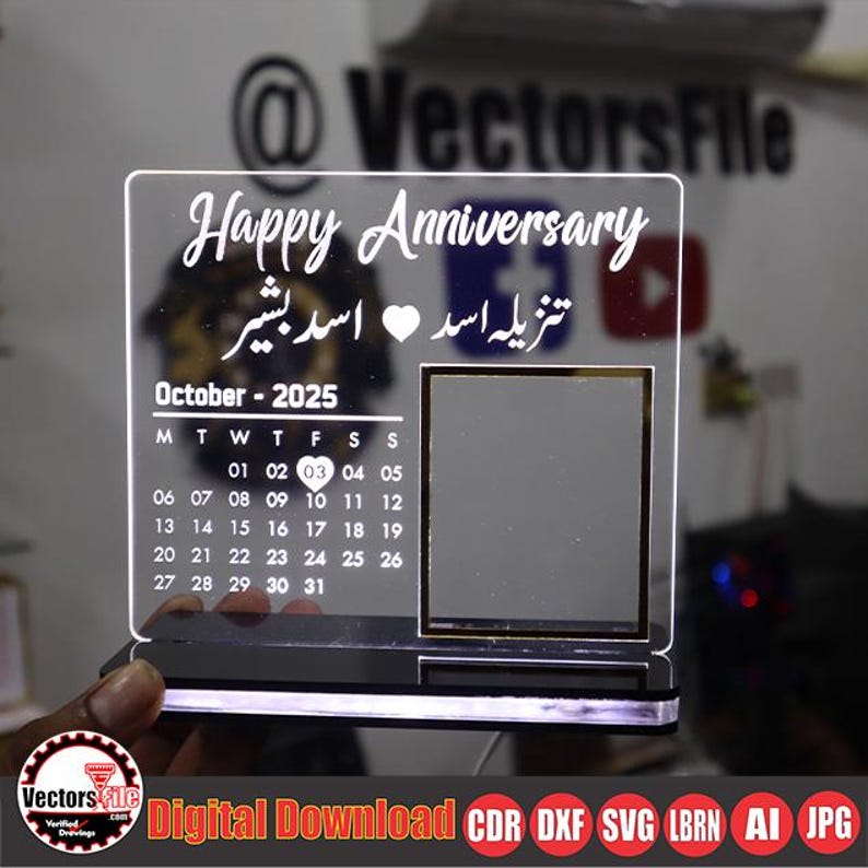May include: A clear acrylic anniversary plaque with the words "Happy Anniversary" and text in a foreign language. The plaque includes a calendar for October 2025 and a photo frame. The base has a black finish with a glowing light.