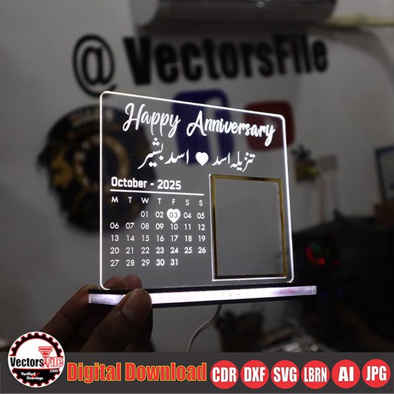 May include: A clear acrylic anniversary plaque with the words "Happy Anniversary" and a calendar for October 2025. The plaque includes a photo frame and the names "Tanzila Asad" and "Asad Bashir". The base of the plaque is illuminated.