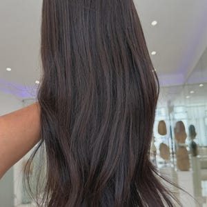 May include: A long, straight wig with a dark brown color. The hair features a smooth texture with slight layering toward the ends, creating a natural flow. The strands are dark, uniform in tone, and reach past the shoulder in length.