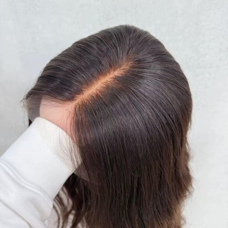 May include: A dark brown wig featuring a lace front construction with a visible center part. The hair is straight and smooth, showcasing a natural-looking scalp area where the individual strands are attached to the sheer lace material.