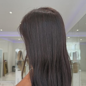 May include: A long, straight hair extension piece in a dark brown shade. The hair is smooth and sleek, featuring a natural-looking texture that flows downward. The strands are uniform in color, providing a consistent appearance from the top to the ends.