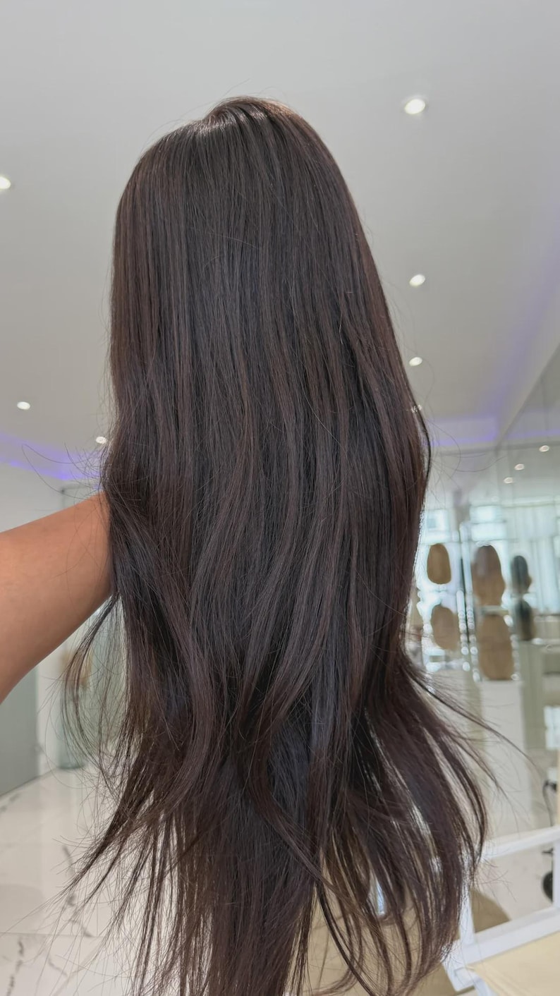 May include: A long, straight wig with a dark brown color. The hair features a smooth texture with slight layering toward the ends, creating a natural flow. The strands are dark, uniform in tone, and reach past the shoulder in length.