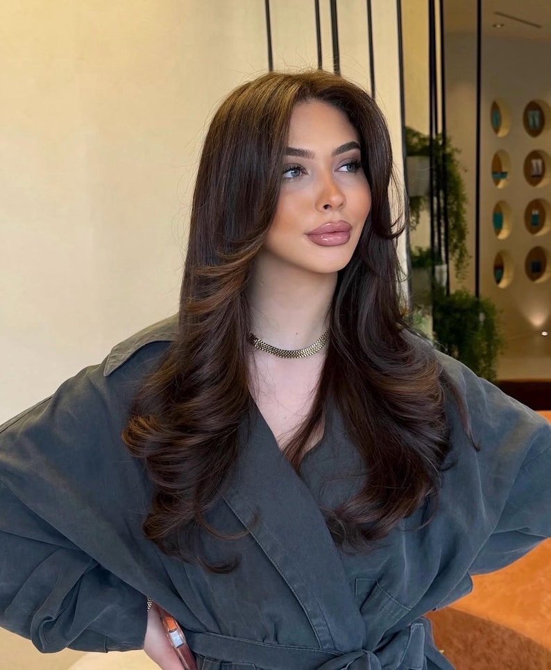 May include: A dark charcoal gray collared jacket with a belted waist and long sleeves, paired with a gold-toned chain link choker necklace. The garment features a structured lapel and a button-down front, providing a clean and uniform appearance.