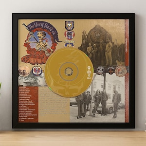 May include: Framed artwork featuring a gold CD and collage elements. The artwork includes the text "The Very Best of Grateful Dead" with a skeleton illustration. The background has vintage photographs and text.