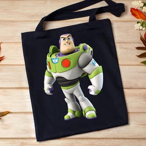 May include: A navy blue tote bag featuring a full-body image of Buzz Lightyear from Toy Story. Buzz is depicted in his signature green, white, and purple spacesuit. The bag has black handles and is made of a sturdy fabric.