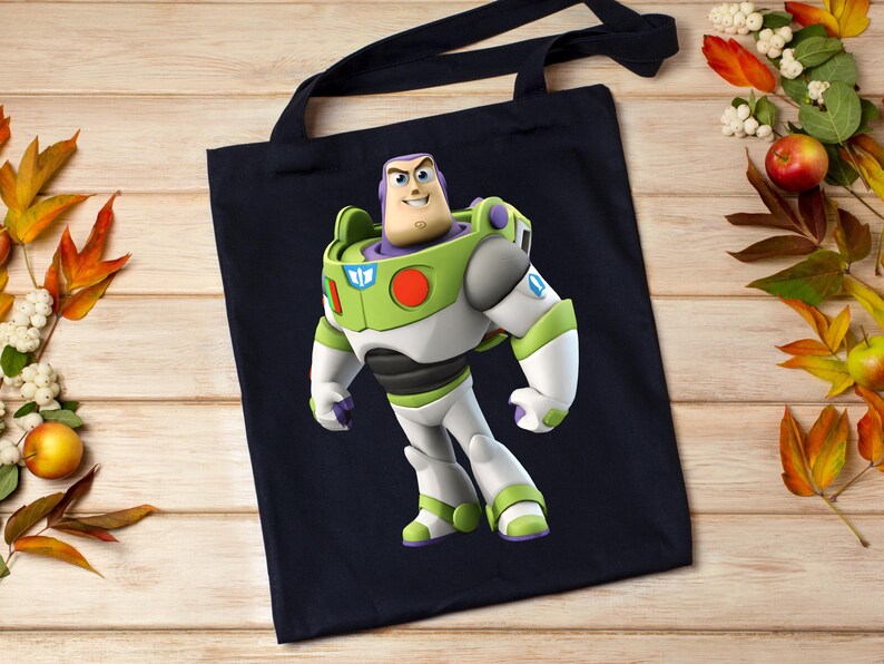 May include: A navy blue tote bag featuring a full-body image of Buzz Lightyear from Toy Story. Buzz is depicted in his signature green, white, and purple spacesuit. The bag has black handles and is made of a sturdy fabric.