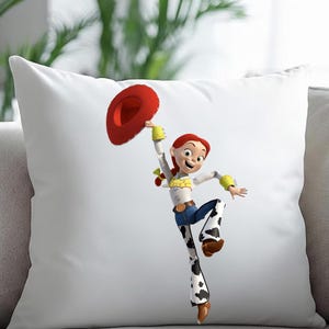 May include: White square pillow featuring a cartoon image of Jessie from Toy Story. Jessie is wearing a white shirt, blue jeans with cow print, and a red cowboy hat. The pillow is on a gray couch.