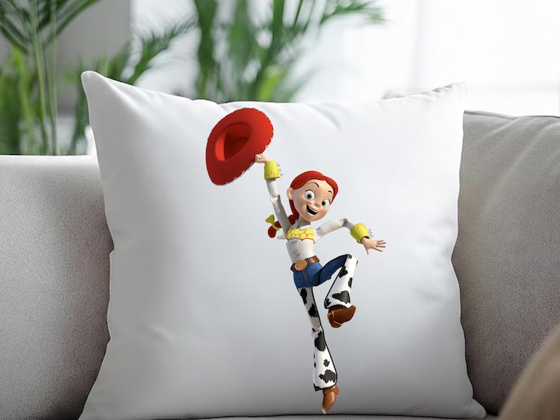 May include: White square pillow featuring a cartoon image of Jessie from Toy Story. Jessie is wearing a white shirt, blue jeans with cow print, and a red cowboy hat. The pillow is on a gray couch.