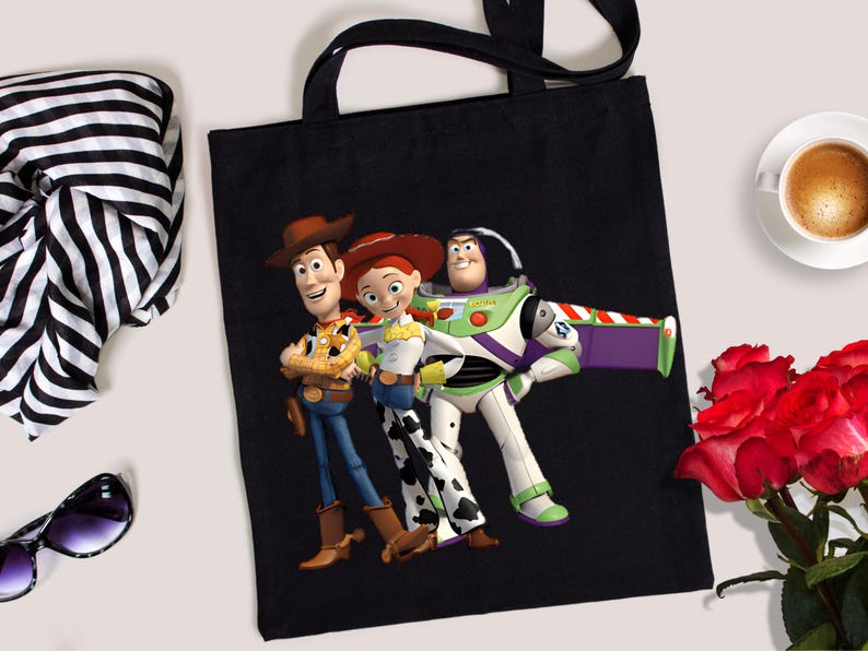 May include: Black tote bag featuring Woody, Jessie, and Buzz Lightyear from Toy Story. The bag has black handles and a colorful graphic of the animated characters. A stylish accessory for fans of the movie.