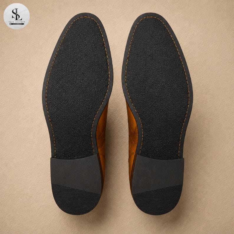 K&ouml;nnte beinhalten: Ein Paar lohfarbene Lederschuhe in der Ansicht von unten, mit schwarzen, strukturierten Au&szlig;ensohlen, sichtbaren N&auml;hten entlang der R&auml;nder und einfarbigen schwarzen Abs&auml;tzen. Die Schuhe sind nebeneinander platziert und zeigen ein klares Design.