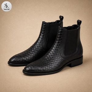 May include: A pair of black leather Chelsea boots with a textured, scale-like pattern. The boots have a pointed toe and a low heel. The elastic side panels and pull tabs provide easy wear. The boots are displayed on a neutral background.