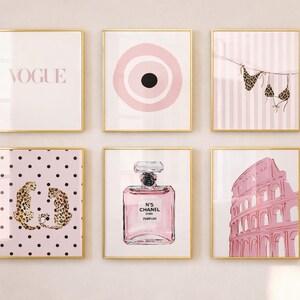 May include: Six framed art prints with gold frames. The prints feature various pink and gold designs, including the word "VOGUE", a target, a bikini, leopard print, a perfume bottle, and the Colosseum.