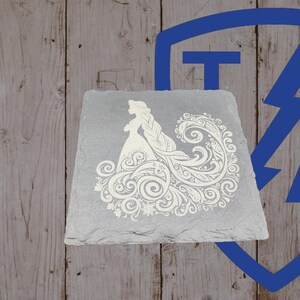 May include: A gray slate coaster featuring a white silhouette of a woman in a flowing gown with intricate floral and swirl designs. The coaster is square with slightly uneven edges, set against a wooden background.