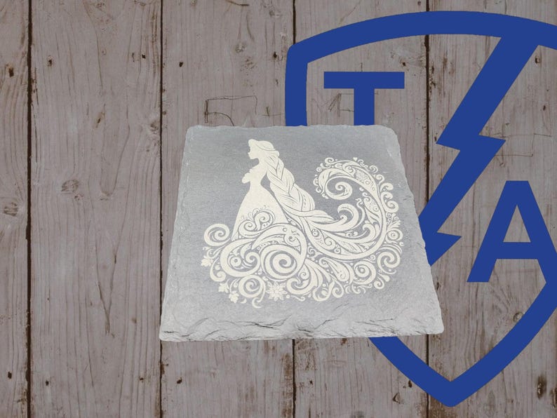 May include: A gray slate coaster featuring a white silhouette of a woman in a flowing gown with intricate floral and swirl designs. The coaster is square with slightly uneven edges, set against a wooden background.