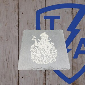 May include: A gray slate coaster featuring a white engraved image of a cartoon character. The character is surrounded by swirling lines. The background is a wooden surface with a blue logo.