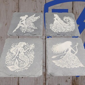 May include: Four gray slate coasters with white etched designs. Each coaster features a different fairytale character: a fairy, a princess, a mermaid, and a warrior princess. The coasters are square with irregular edges.