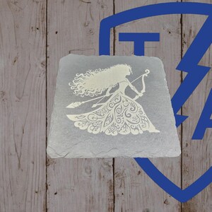 May include: A gray, rectangular slate stone features a white silhouette of a woman with long flowing hair, holding a bow and arrow. The woman is wearing a detailed dress. The background is a wooden surface.