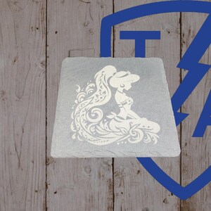 May include: A square, gray slate coaster featuring a white silhouette of a woman with long hair and a decorative dress. The design is detailed with swirling patterns. The coaster sits on a wooden surface.