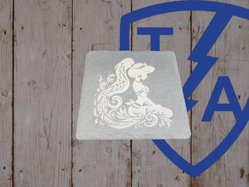 May include: A square, gray slate coaster featuring a white silhouette of a woman with long hair and a decorative dress. The design is detailed with swirling patterns. The coaster sits on a wooden surface.
