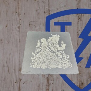 May include: A square, gray slate coaster featuring a white, ornate design of a couple, possibly from a fairy tale. The design includes floral elements and detailed figures. The coaster is set against a wooden background.