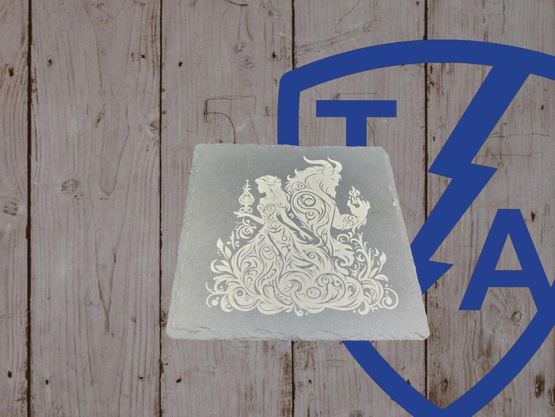 May include: A square, gray slate coaster featuring a white, ornate design of a couple, possibly from a fairy tale. The design includes floral elements and detailed figures. The coaster is set against a wooden background.