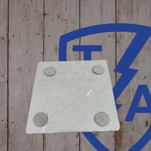May include: A square, light gray stone coaster with four small, round, gray pads on the underside. The coaster is set against a light brown wooden background with a blue graphic in the upper right corner.