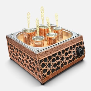 May include: A square copper-colored coffee sand heater featuring an intricate black geometric lattice pattern on the sides, containing five hammered copper coffee pots and five matching gold-toned metal spoons resting in a bed of sand.