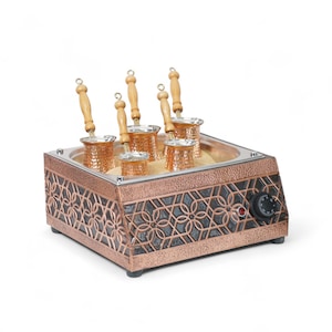 May include: A copper-colored electric coffee maker with six copper coffee pots with wooden handles. The coffee maker has a decorative geometric pattern on the sides and a control knob. The pots are set in sand.
