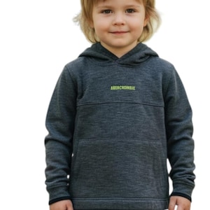 May include: A young child wearing a dark gray Abercrombie hoodie with a front pocket and the brand name in neon green. The child is also wearing blue jeans. The hoodie has a hood and long sleeves.