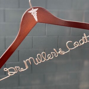 May include: A brown wooden hanger with a white medical symbol and the text "Dr. Miller's Coat" in white wire.