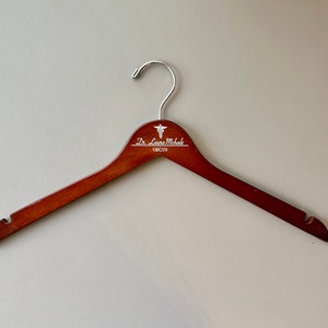 May include: A brown wooden hanger with a silver hook and a white inscription that reads "Dr. Laura Michale OB/GYN" with a medical symbol.