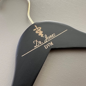 May include: Black wooden hanger with a gold inscription that reads "Dr. Jones DVM" and a gold medical symbol.