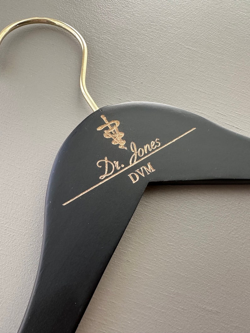 May include: Black wooden hanger with a gold inscription that reads "Dr. Jones DVM" and a gold medical symbol.