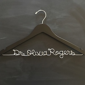 May include: Black wooden hanger with a silver wire inscription that reads "Dr. Olivia Rogers".