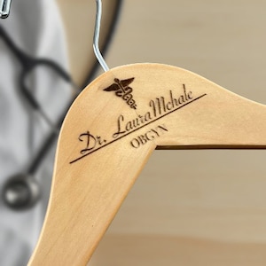 May include: A wooden hanger with a personalized inscription that reads "Dr. Laura Michale OBGYN" and a medical symbol.