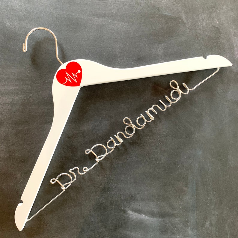 May include: White wooden hanger with a red heart and a silver wire inscription that reads "Dr. Dandamudi".