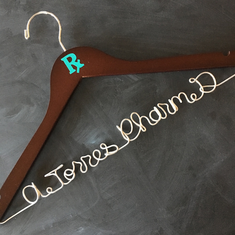 May include: A brown wooden hanger with a turquoise "R" on the top and the words "Dr. Torres Pharmacy" written in silver wire.