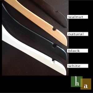 May include: Four wooden hangers in different colors: walnut, natural, black, and white. The hangers are stacked on top of each other.