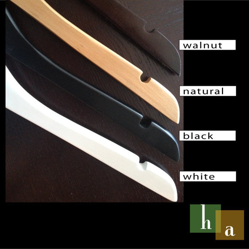 May include: Four wooden hangers in different colors: walnut, natural, black, and white. The hangers are stacked on top of each other.